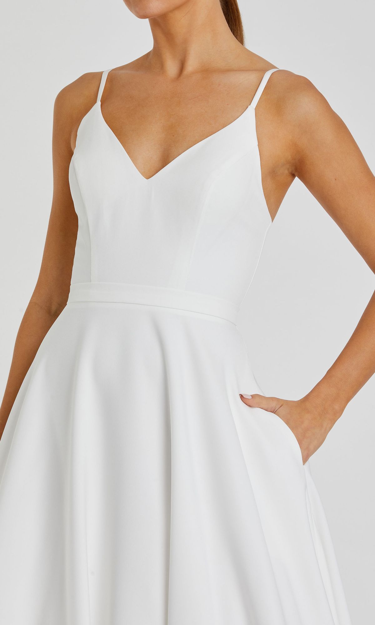 A woman models the Classic Long A-Line Formal Dress: Mac Duggal 48855, a sleeveless white gown with a fitted bodice, flared skirt, thin straps, and pockets.